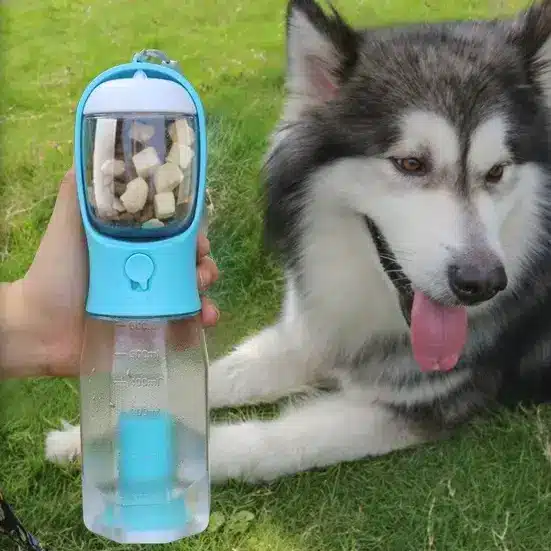 3-in-1 Leak-Proof Travel Bottle & Feeder for Pets 2 A Hand Holding A Blue Water Bottle With A Built-In Food Dispenser Next To A Large, Fluffy Dog.