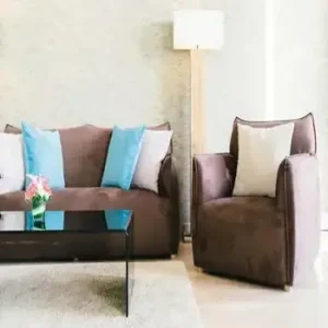 A brown sofa with blue and white cushions next to a matching armchair and a glass coffee table.