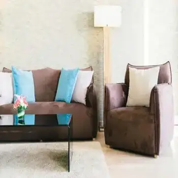 A brown sofa with blue and white cushions next to a matching armchair and a glass coffee table.