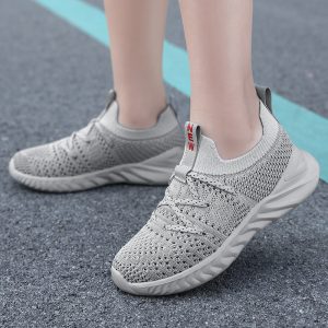 Comfortable grey athletic sneakers on person's feet, showcasing breathable knit fabric, cushioned soles, and modern design for active lifestyles and sneaker enthusiasts.