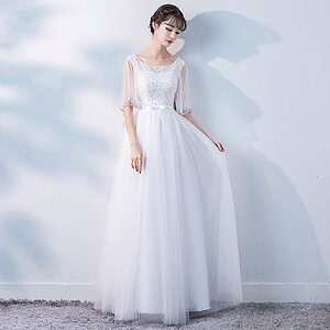 A woman wearing a white long sleeve evening dress with a beaded bodice and flowing skirt.