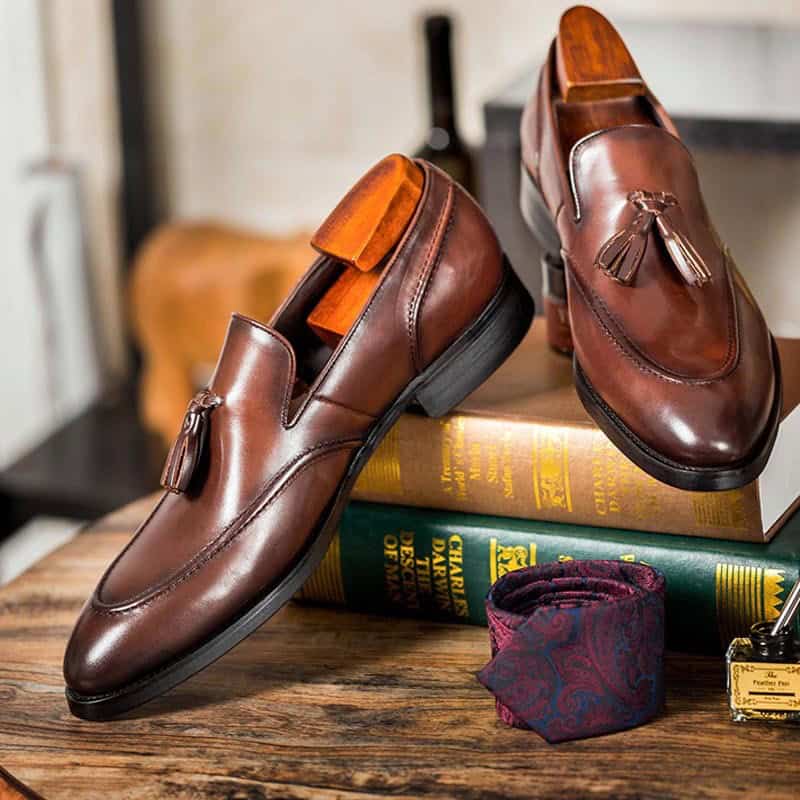 Timeless Elegance: Stylish Tassel Leather Shoes for Today's Gentleman 3 Elegant Men'S Brown Leather Tassel Loafers Displayed On Vintage Books With A Wooden Shoe Tree Inside, Showcasing Luxury Footwear And Accessories.