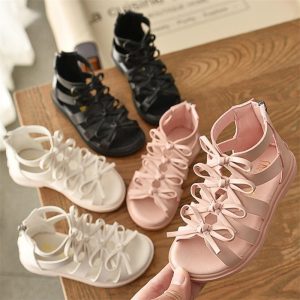 Colorful lace-up sandals for women, in black, white, and pink, displayed on a wooden surface, perfect for casual and stylish summer fashion.