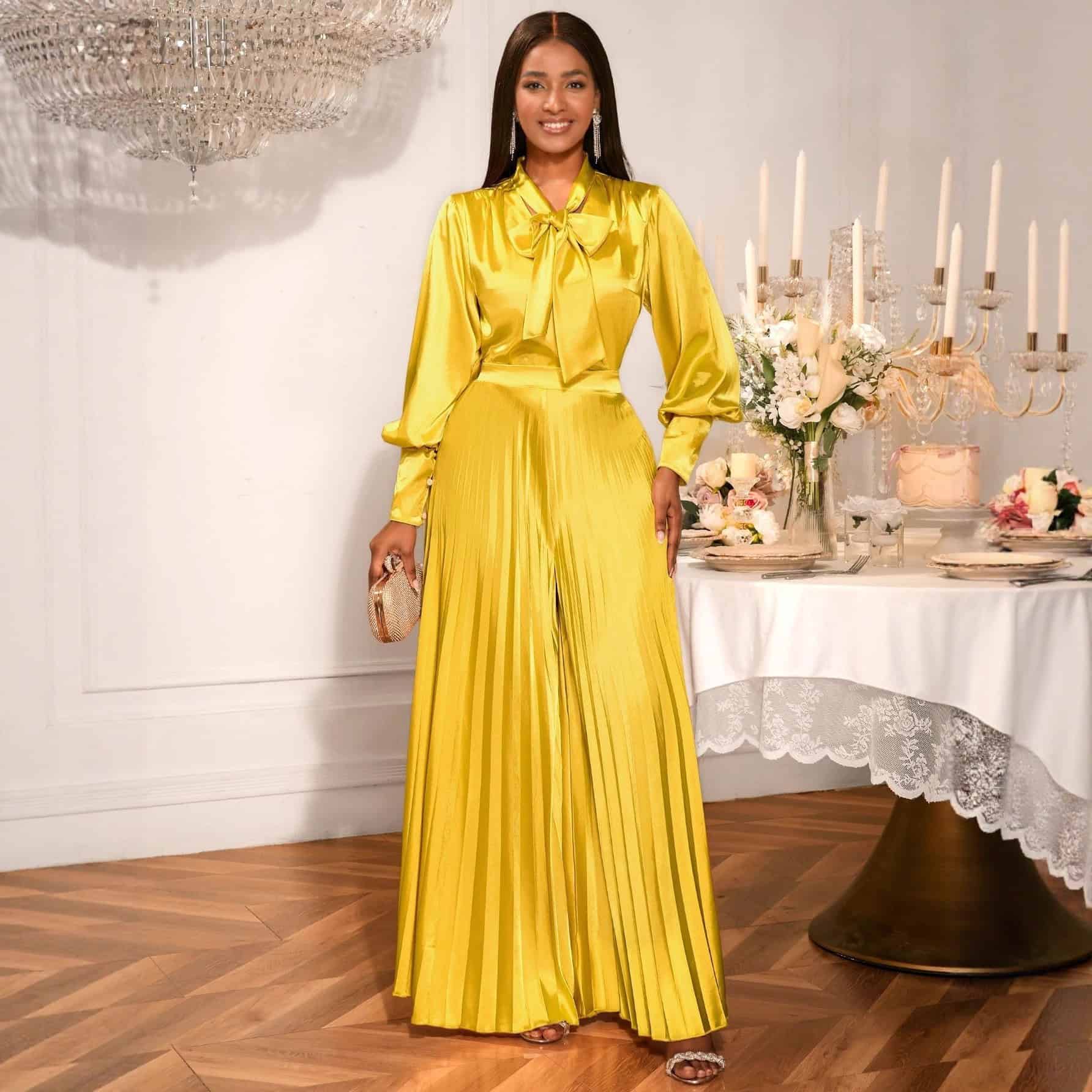 Chic V-neck Top & Wide Leg Trousers Set with Bow Detail - Elegant Fashion Combo 1 Woman Wearing A Yellow Satin Jumpsuit With A Bow Tie And Pleated Design, Standing Beside A Table With Candles.