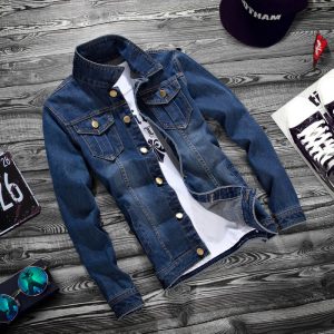 Blue denim jacket with button closures and a collar laid flat on a wooden surface.