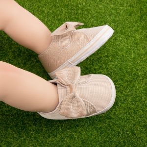 Soft beige mesh sneakers with bow detail on green grass, casual athletic footwear, stylish comfortable shoes, trendy sneakers for women, lightweight and breathable sports shoes.