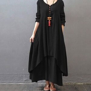 A woman wearing a black long sleeve dress with an asymmetrical hem and a red pendant necklace.