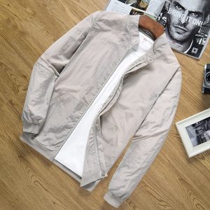 Soft beige men's bomber jacket with white inner lining and ribbed cuffs, stylish casual outerwear for spring and fall, displayed on a wooden surface with magazines and photo frames for a modern fashion look.