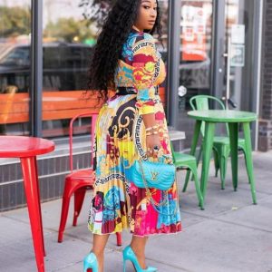 Woman wearing a colorful printed dress and blue high heels, standing outside near chairs.
