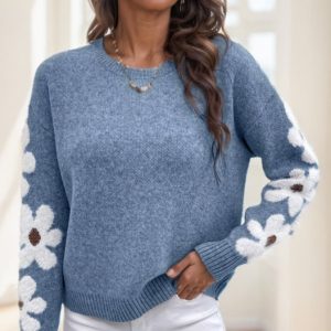 Blue sweater featuring white floral patterns on the sleeves and a round neckline.