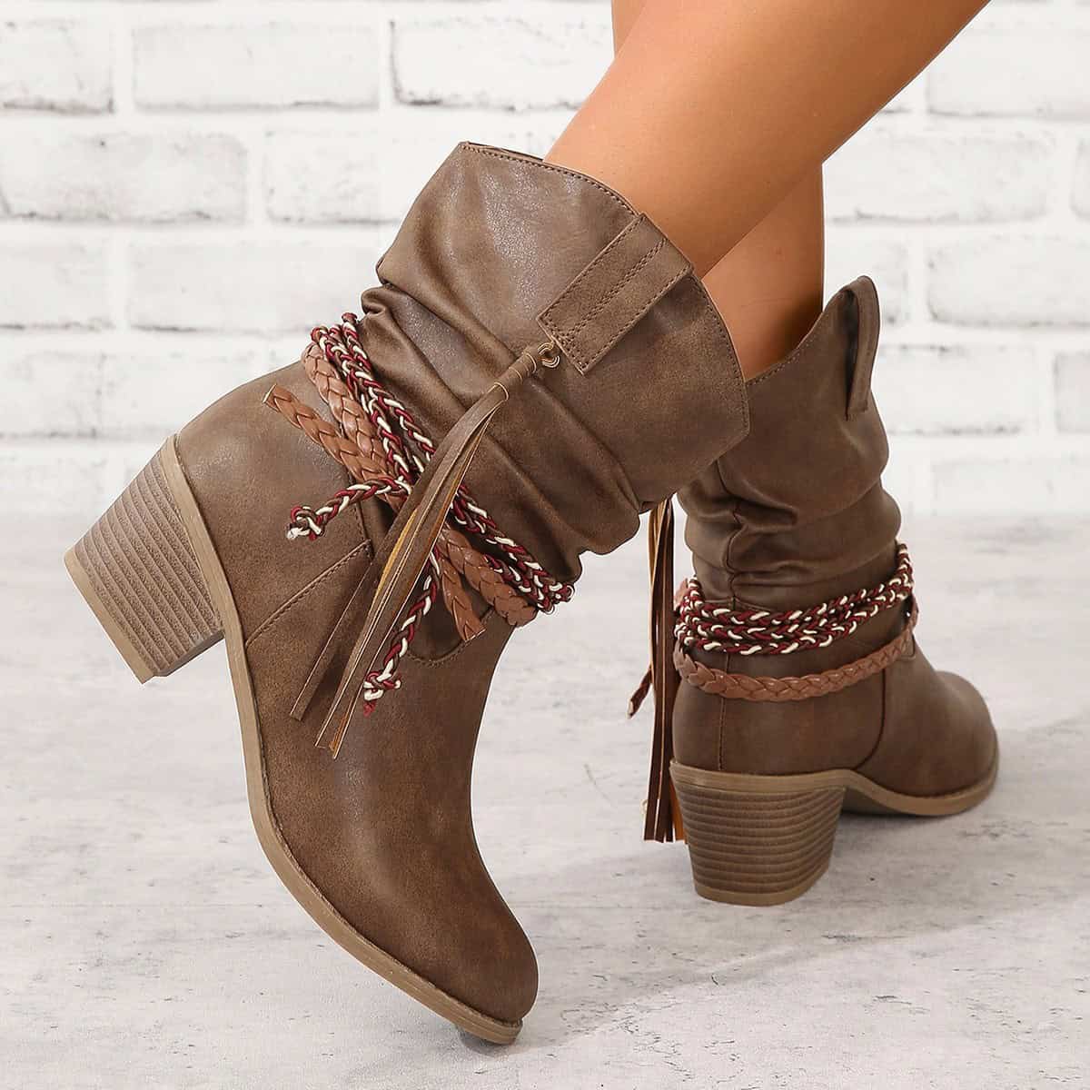 Vintage Western Tassel Mid-Calf Boots - Winter Chic Appeal 2 Trendy Brown Ankle Boots With Chunky Heels, Stylish Braided And Rope Laces, Perfect For Fall Fashion And Casual Wear, Displayed Against A White Brick Background.