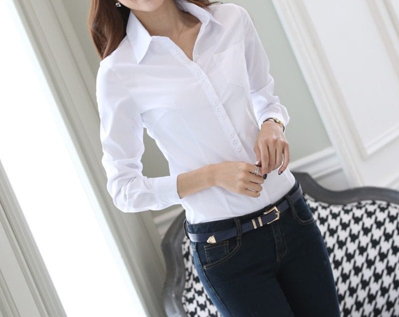 Elegant Women's Slim Fit Professional Shirt - Long-Sleeved Tailored Style 5 Woman Wearing A White Button-Up Shirt With Long Sleeves And Dark Jeans, Standing Indoors.