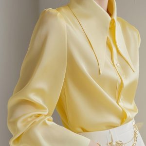 Close-up of a yellow satin blouse featuring a large collar and button details.