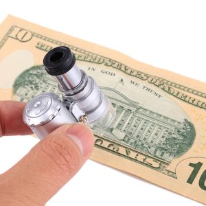 A person holding a handheld magnifying glass over a ten-dollar bill featuring the U.S. Capitol.