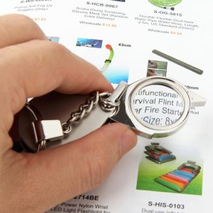 Hand holding a multifunctional survival flint fire starter with a magnifying glass attached.