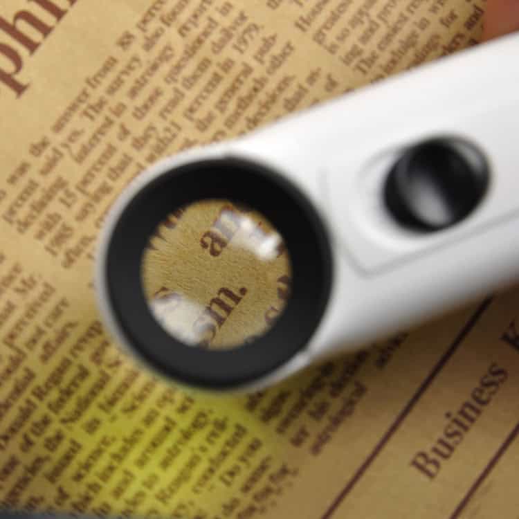 Exclamation Mark Style Magnifier: 40X Handheld with 2-LED Light 5 Close-Up Of A Magnifying Glass Focusing On Printed Text On A Newspaper Page.