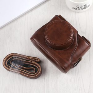 Brown leather camera bag with adjustable strap on a white surface, next to a coffee mug with "Good Morning" text. Stylish travel accessories for photography enthusiasts and travelers.