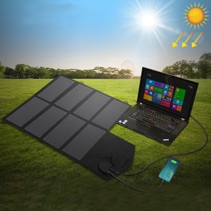 Solar-powered laptop charging setup on grass with solar panel, portable charger, and Windows laptop under sunny sky.