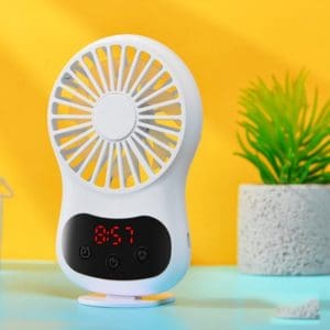 White portable desk fan with a digital clock display and a small plant in the background.