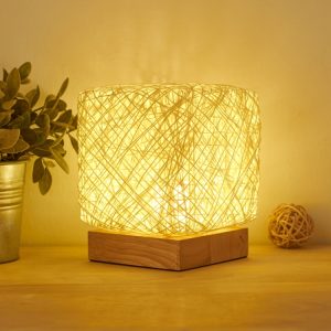 A decorative table lamp with a woven shade emitting warm light, placed on a wooden surface.