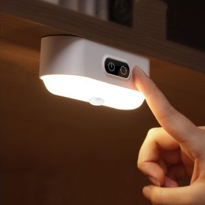 A hand pressing the button on a touch-activated LED light mounted under a cabinet.