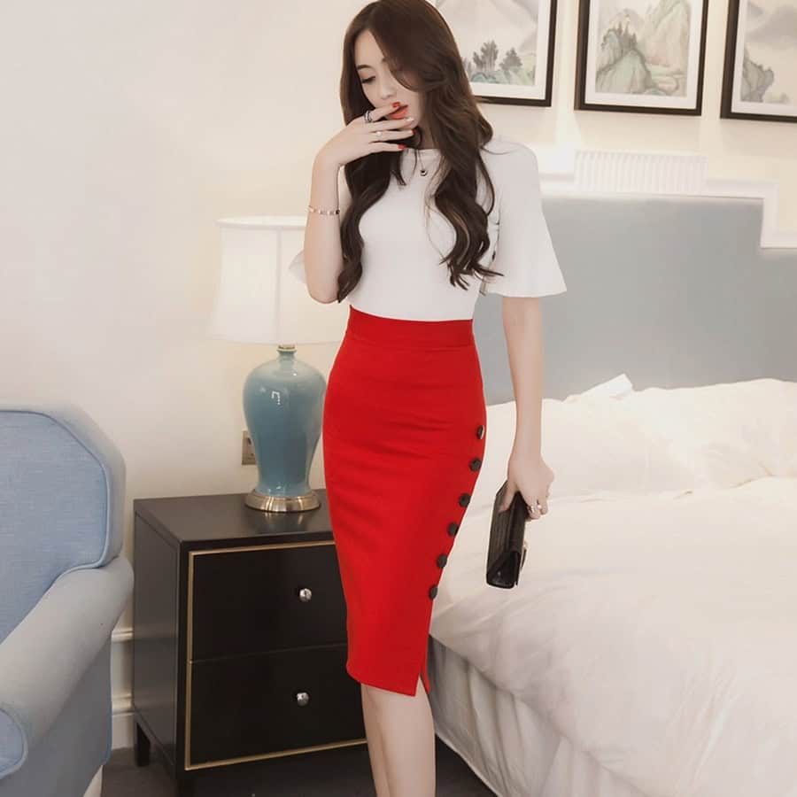 Elegant Split Skirt - Sophisticated Hip Skirt for Stylish Statements 1 Elegant Woman In Stylish White Top And Red Pencil Skirt With Black Buttons, Holding Clutch, Posing In Modern Bedroom With Framed Artwork, Showcasing Fashion And Style From Syndmart.