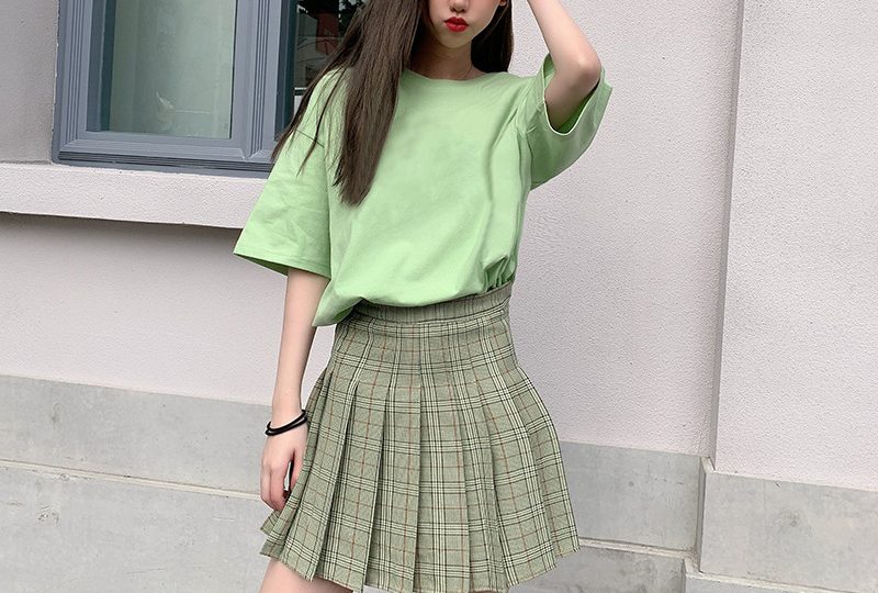 Classic Round Neck Drop Shoulder T-Shirt - Comfort meets Style! 4 A Person Wearing A Green T-Shirt And A Plaid Skirt, Posing With One Hand On Their Head.