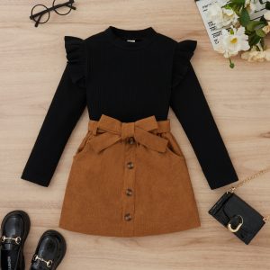 Stylish Women'S Outfit Featuring A Black Ribbed Sweater With Ruffle Shoulder Details And A High-Waisted Brown Corduroy Skirt With Front Buttons And A Bow Belt, Perfect For Fall Fashion.
