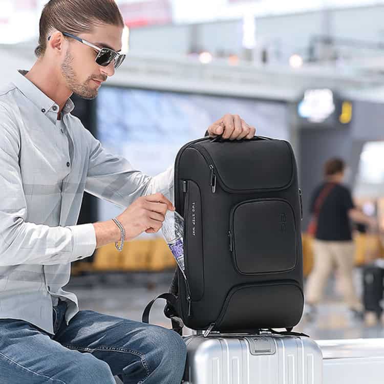 BANGE BG-7216plus 15.6" Laptop Antitheft Travel Backpack: Waterproof & Durable 6 Suitcase With A Black Travel Backpack And A Silver Carry-On At An Airport, Emphasizing Durable Travel Gear And Baggage Essentials For Travelers.