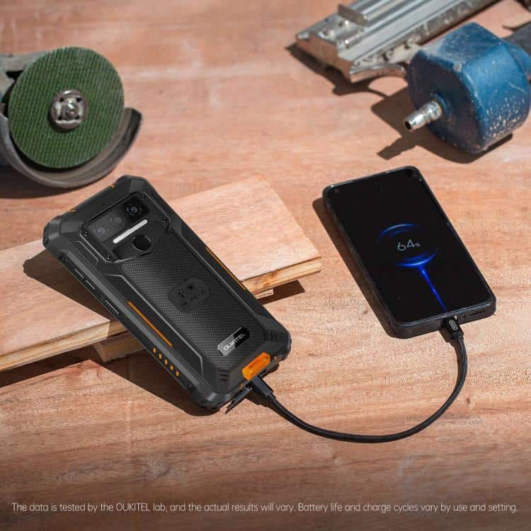 Oukitel WP23 Plus: Rugged 6.52" 8GB+256GB Android 14.0 NFC Octa-core 4G Phone 8 Rugged Smartphone Connected To A Charging Cable On A Workbench With Tools In The Background.