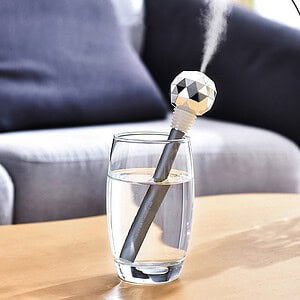 Floating solar-powered Sterling light bulb shaped diffuser in a glass of water, providing ambient scent or aromatherapy for home relaxation.